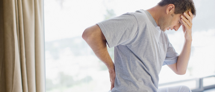 man knealing holding his lower back with one hand, and his head with the other hand