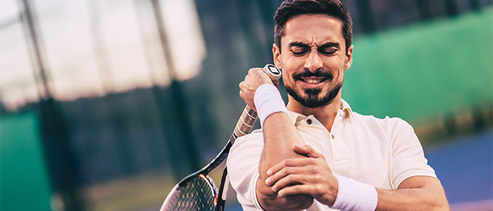 A man holding his right elbow in pain with a tennis racket in his right hand